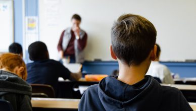 Alumnado dando la espalda y fondo desenfocado con profesor