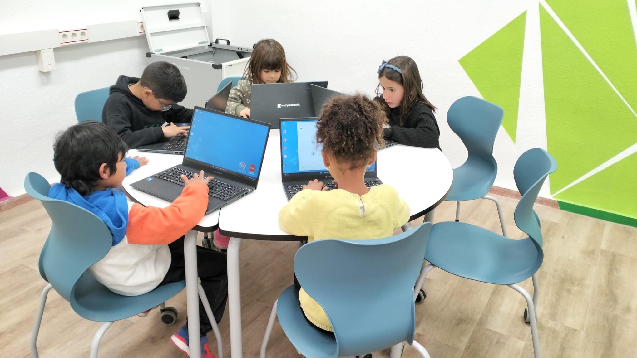 Grupo de alumnos y alumnas trabajando con portátiles en mesas reconfigurables