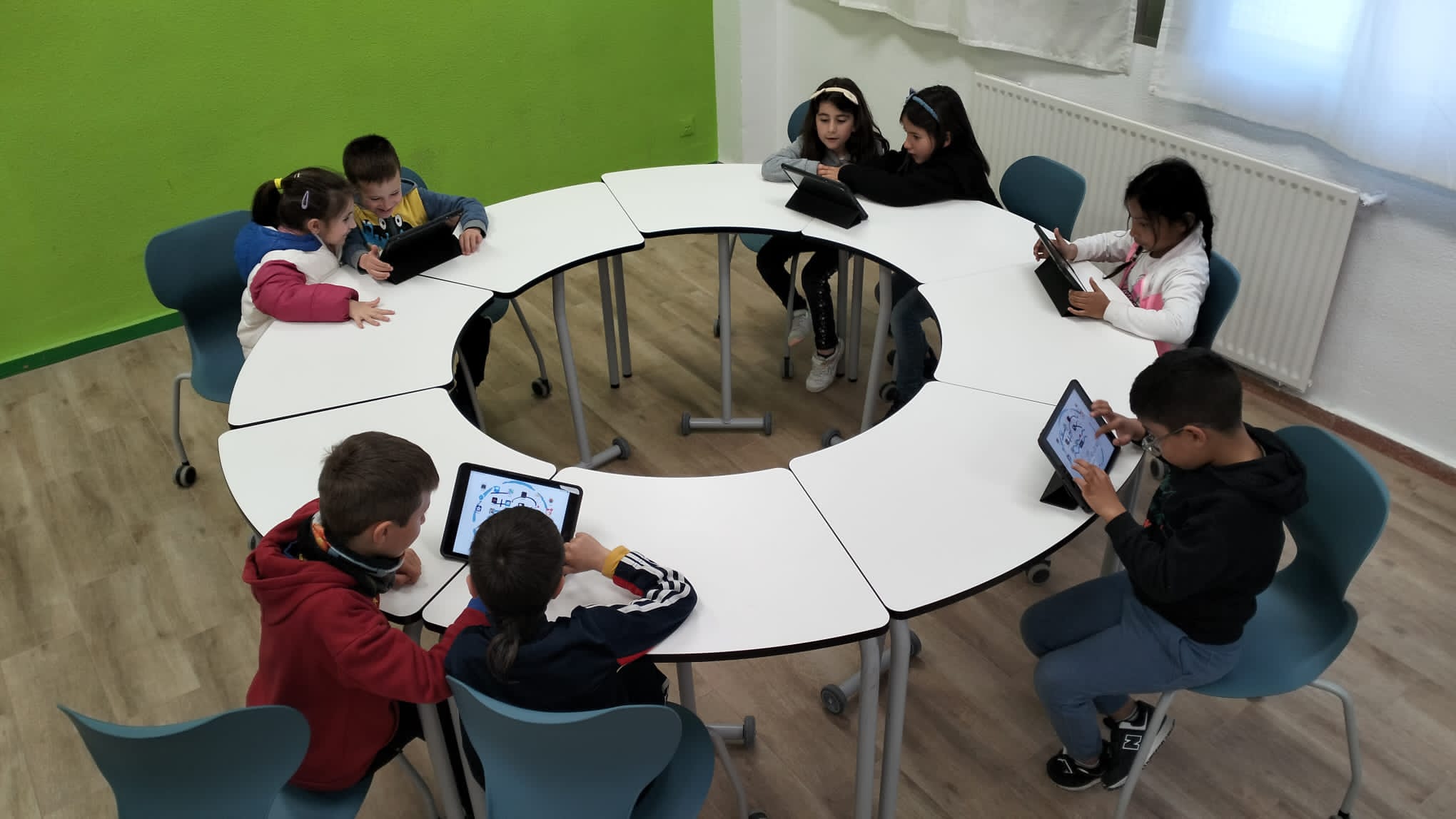 Grupo de alumnos y alumnas trabajando con tablets en mesas reconfigurables