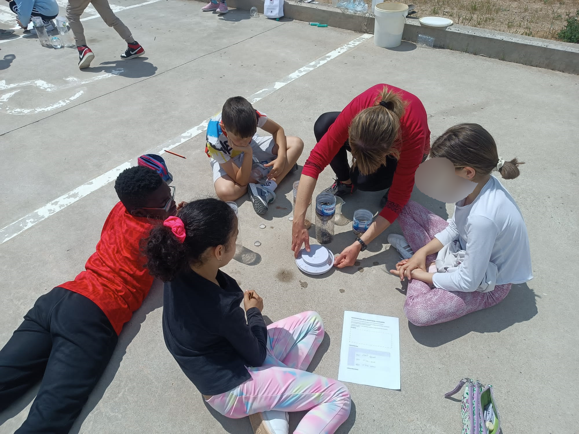 Estudiantes sentados en el suelo del patio haciendo una actividad sobre las características de los materiales